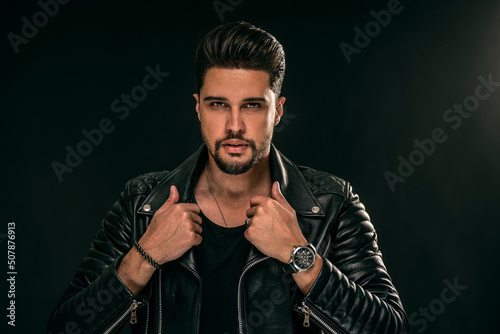 Portrait of a handsome young man with manly face. Male beauty. Fashionable brunet guy in black leather jacket looking at the camera.
