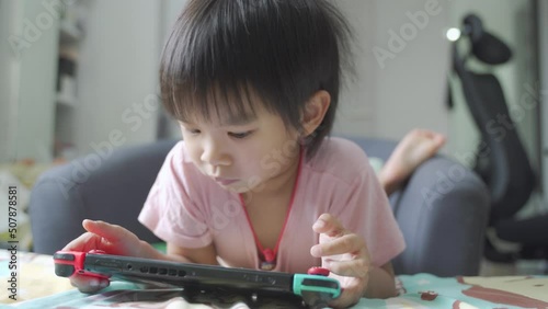 Little boy lying in bed and playing a video game on portable mobile game or mobile phone while spending free time at home