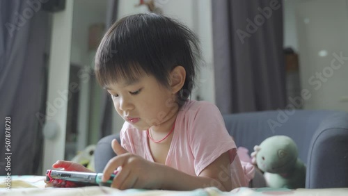 Little boy laying in bed and playing a video game on a portable mobile game or mobile phone while spending free time at home