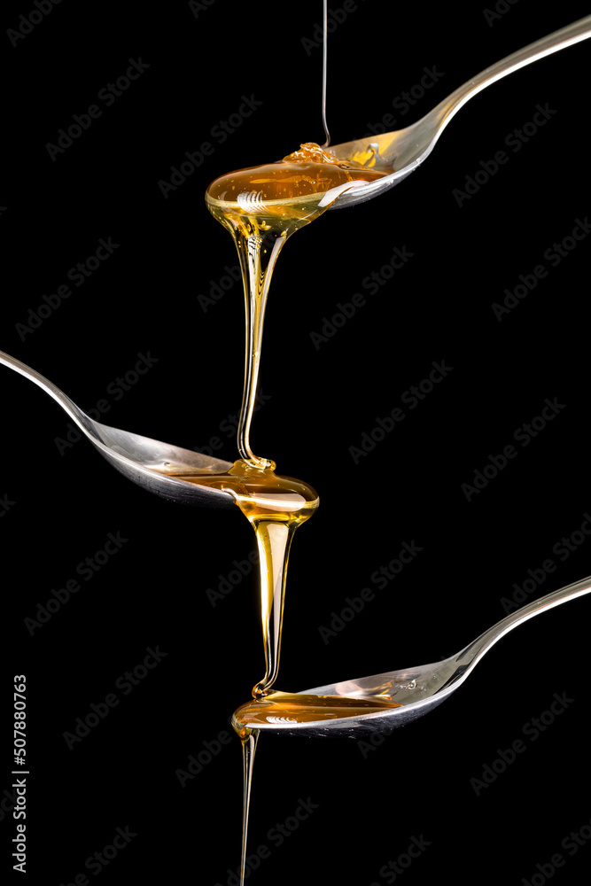 Φωτογραφία Honey dripping in silver spoon, black background.