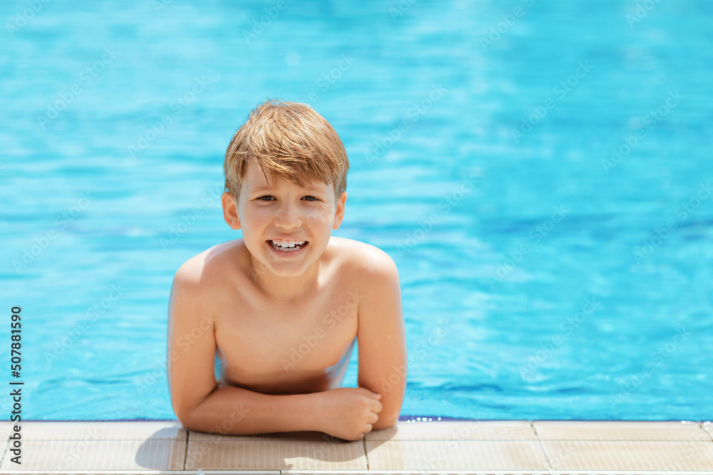Smiling cute little boy in outdoor swimming pool in sunny day. Summer activities for kids at holidays.