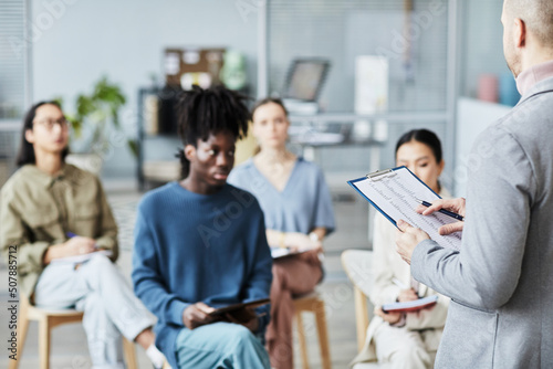 Back view of male coach giving lecture or seminar in office to diverse group of people, copy space