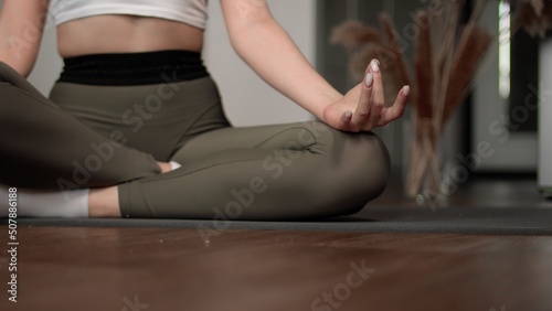 Close-up of an unrecognizable woman doing yoga while sitting on the floor in the lotus position at home in the living room. Just relaxation and meditation.