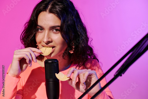 Billede på lærred Portrait of modern young woman sitting at desk in studio in pink neon light biti