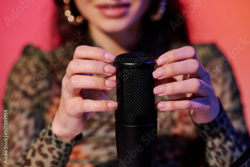 Selective focus of young blogger sitting in studio in pink and yellow neon light recording sounds for ASMR vlog scratching and tapping microphone photo