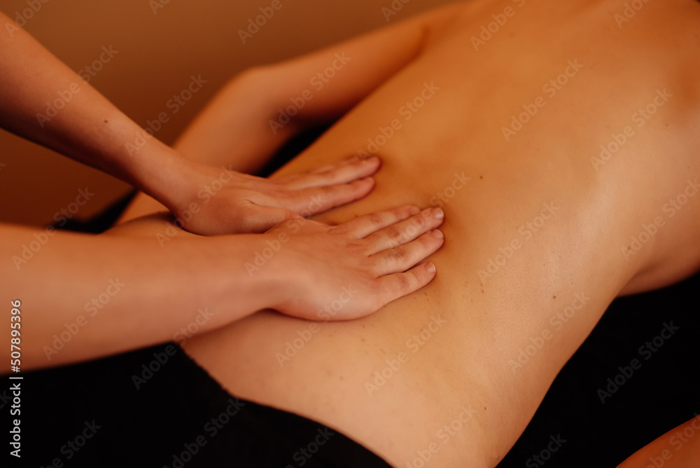 Detail of the hands of a therapist doing a massage on the back of an unrecognizable woman.
