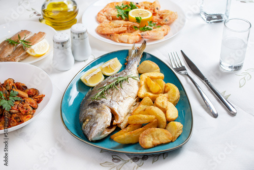 Traditional Greek food, Dorada fish with Greek salad, Mediterranean traditional menu, Grilled sea bream, shrimps or prawns zucchini, variety of seafood, mussels, tzatziki, potatoes, feta and ouzo