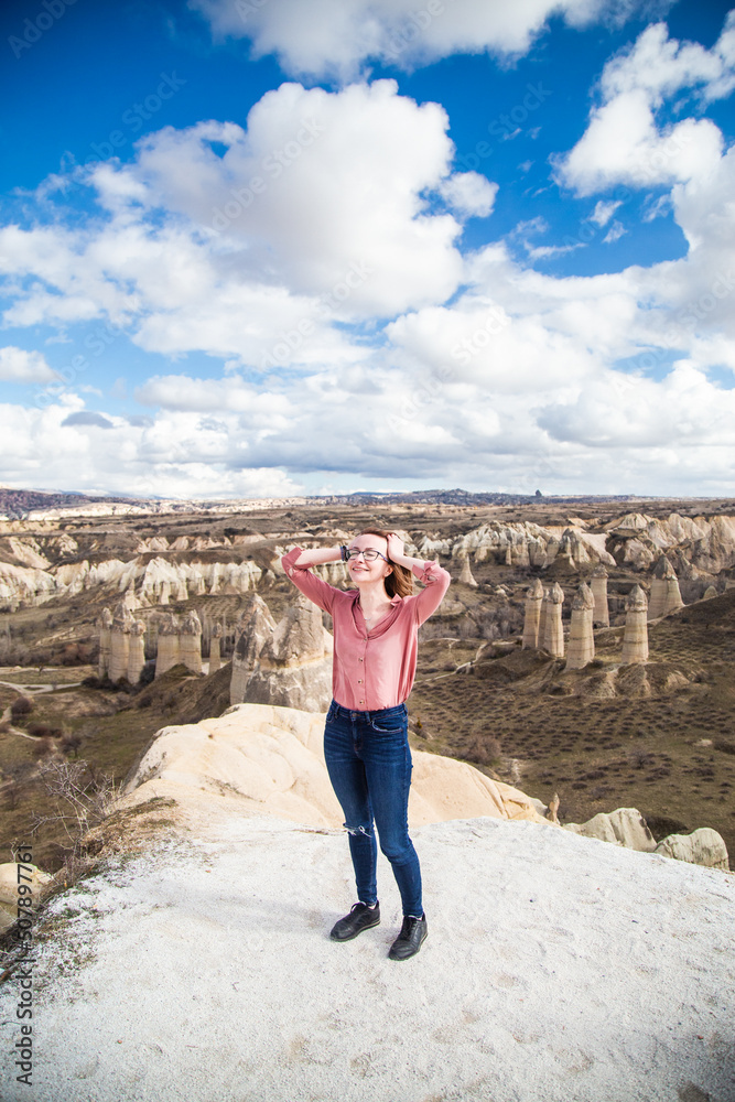 Naklejka premium Young happy woman traveler enjoying a vacation in desert Cappadocia Turkey. Tourist girl active lifestyle outdoor portrait. Female portrait in the valley of love Cappadocia