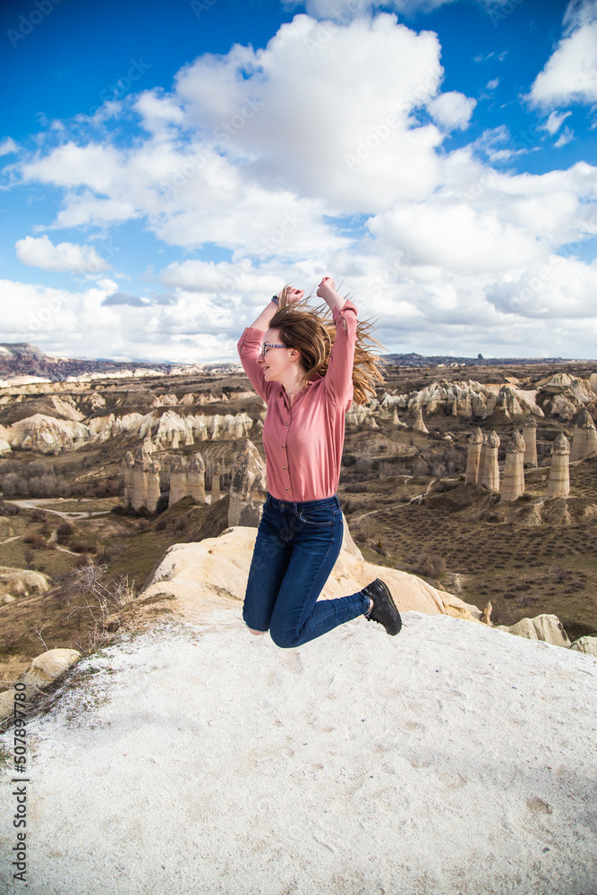 Young happy woman traveler jumping enjoying a vacation in desert Cappadocia Turkey. Tourist girl active lifestyle outdoor portrait. Female portrait in the valley of love Cappadocia