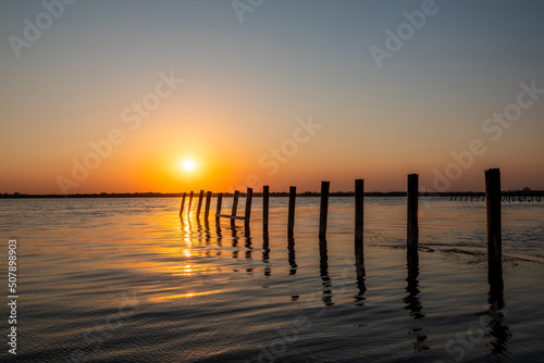 Fototapeta Naklejka Na Ścianę i Meble -  Beautiful red and orange sunset over the sea. The sun goes down over the sea. A flock of cormorants sits on a old sea pier in orange sunset light
