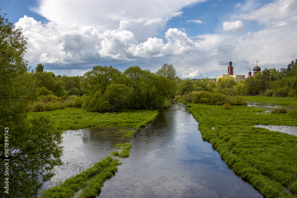 It's raining on a bright sunny day. Rural landscape with river and green grass and trees. Juicy greenery in mushroom rain It's raining on a bright sunny day. Rural landscape with river and green grass and trees. Juicy greenery in mushroom rain