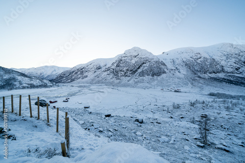 white snow-capped Norwegian mountains with a fence and a frozen lake in the distance © Rolands