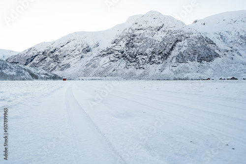 snowy norwegian mountains with a small red house in the distance to which the road leads