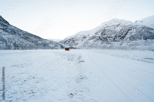 snowy norwegian mountains with a small red house in the distance to which the road leads