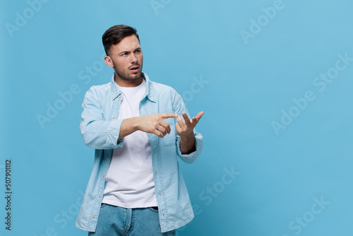 Concentrated pensive tanned handsome man in casual basic t-shirt counts on his fingers posing isolated on blue studio background. Copy space Banner Mockup. People emotions Lifestyle concept