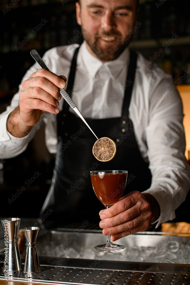 bartender holds wineglass with cocktail and garnishes it with a slice of dry lemon
