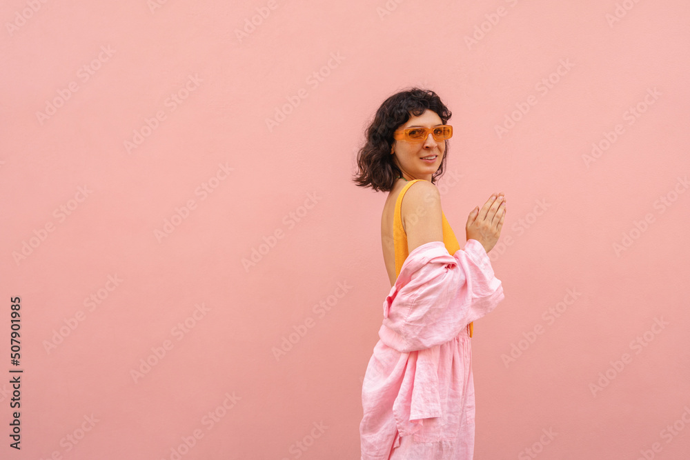 Fashionable young brunette caucasian woman poses for camera on pink background with space for text. Model is wearing summer casual clothes. Concept of enjoying weekends, vacations Fashionable young brunette caucasian woman poses for camera on pink background with space for text. Model is wearing summer casual clothes. Concept of enjoying weekends, vacations
