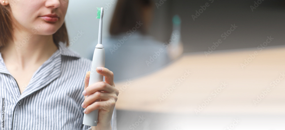 banner of Happy healthy smiling woman with ultrasonic electric brush in bathroom at home. Dental hygiene and teeth care. copy space - obrazy, fototapety, plakaty 