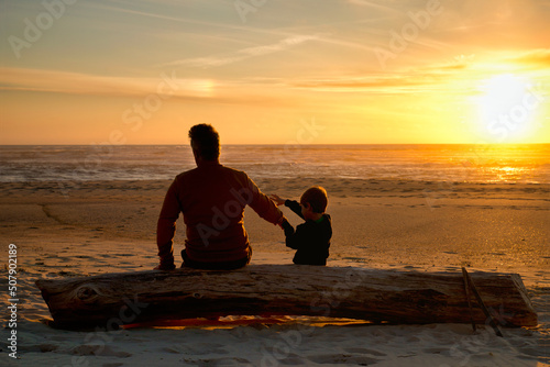 Father and son sit on a trunk on the beach at sunset
