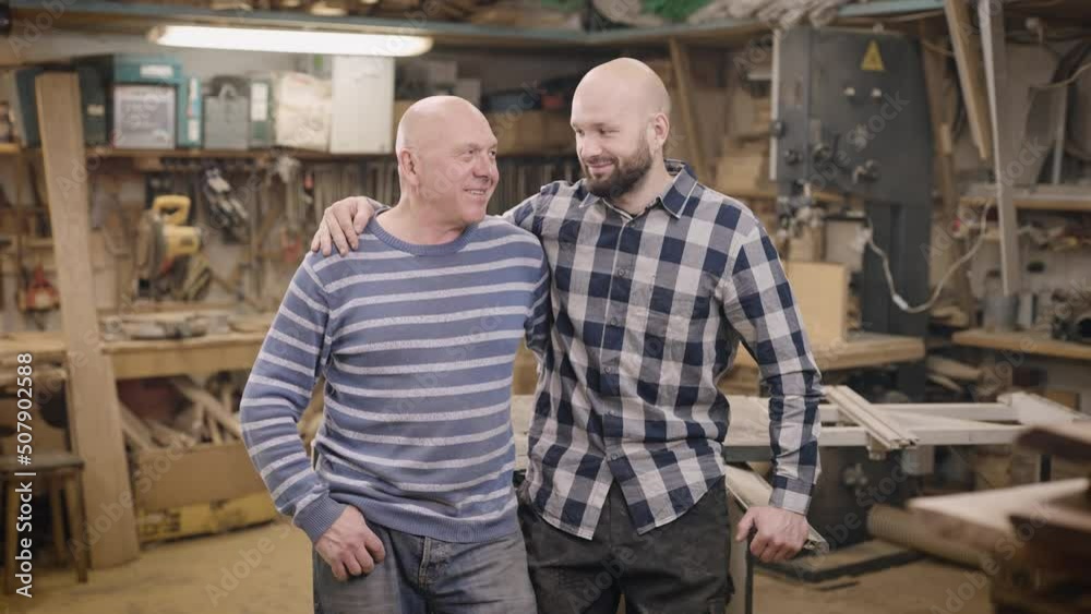 Father and son in their family carpentry workshop. The father passes on his experience and business to his son. Father and son in their family carpentry workshop. The father passes on his experience and business to his son.