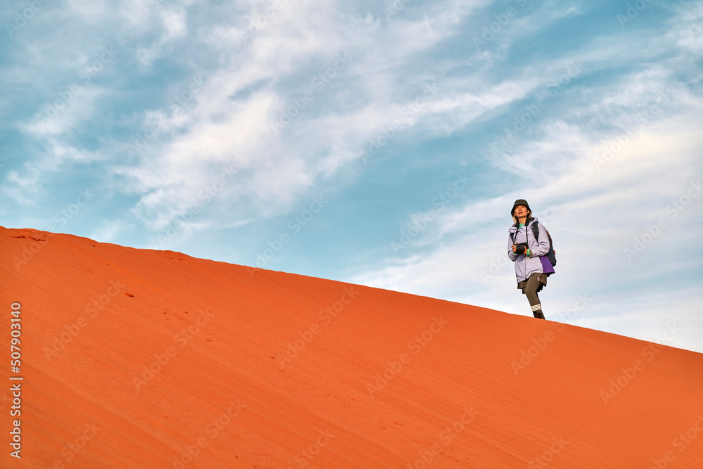 asian female photographer walking on ridge of sand dune