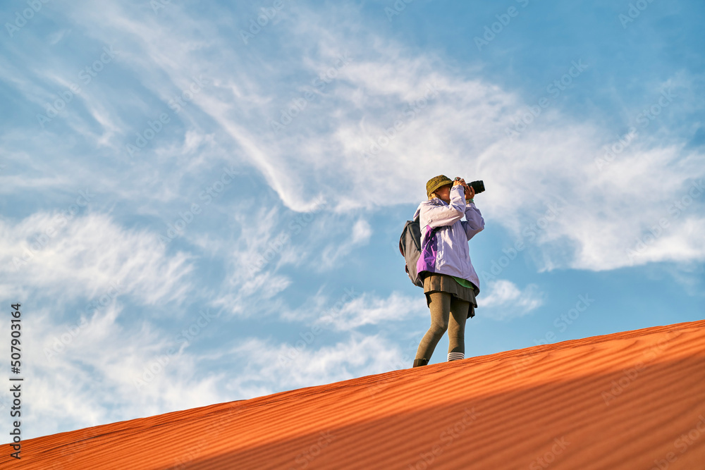 asian woman photographer taking a photo on top of a sand dune asian woman photographer taking a photo on top of a sand dune