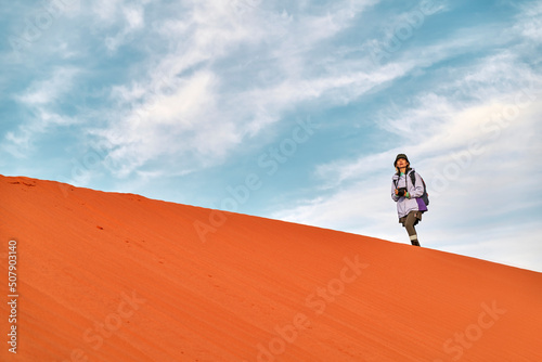 asian female photographer walking on ridge of sand dune photo