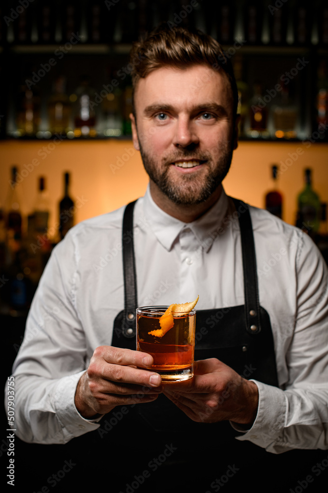 bartender holds transparent glass of alcoholic cocktail garnished with orange peel