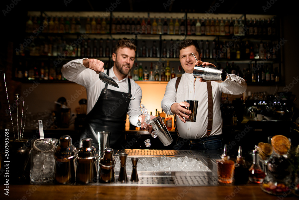 beautiful view on two male bartenders are preparing cocktails in shakers at bar