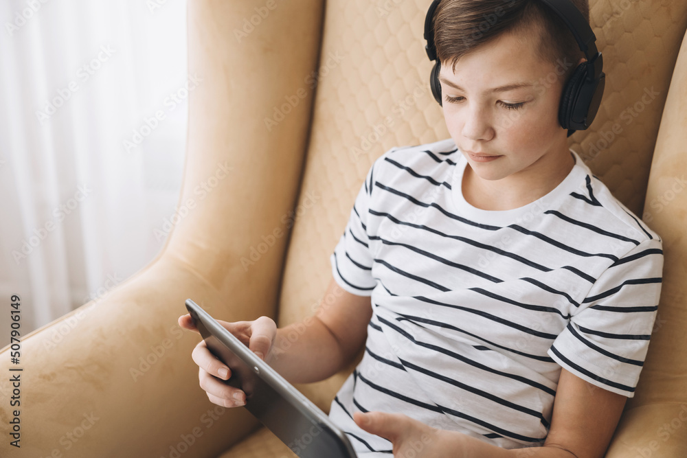 Teenage boy in wireless headphone using tablet having video chat on internet online at home. Child watching movie, playing video game. Social media concept. Online education. Distance learning Teenage boy in wireless headphone using tablet having video chat on internet online at home. Child watching movie, playing video game. Social media concept. Online education. Distance learning