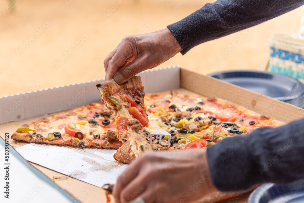 Hands of a hungry party goer pulls one slice of pizza out of the box to eat