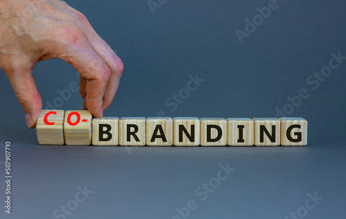 Branding or co-branding symbol. Businessman turns wooden cubes and changes the word Branding to Co-branding. Beautiful grey table grey background, copy space. Business branding co-branding concept. photo