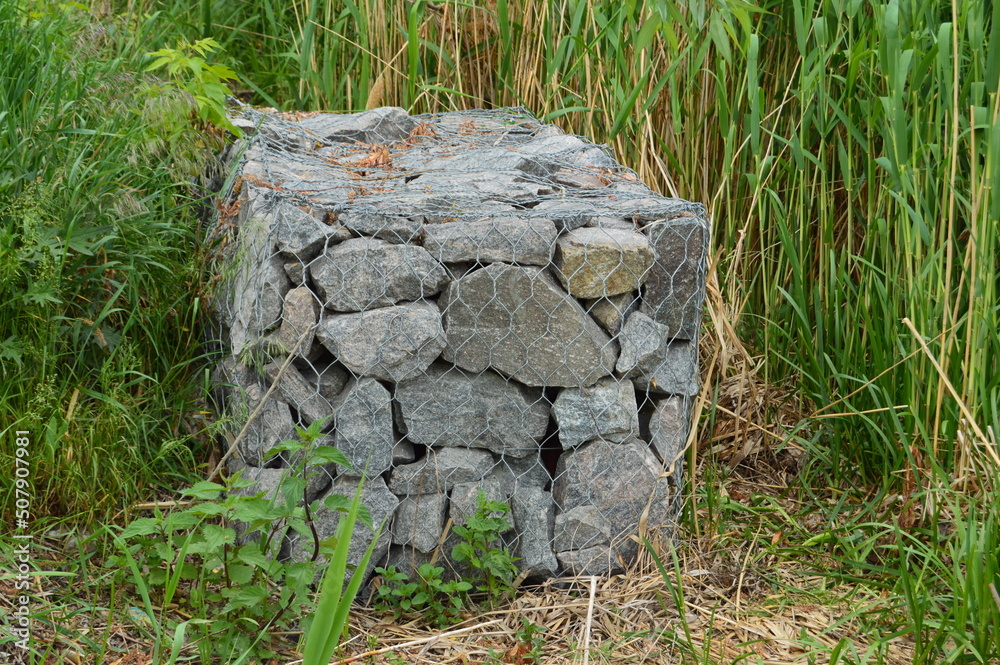 Obraz premium stones in a metal grid near the river