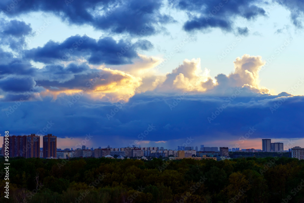 A blue cloud pours rain on the city from above illuminated by the sun