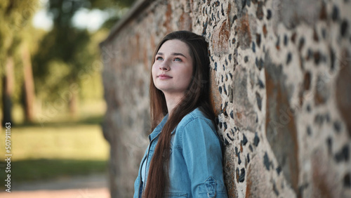 Portrait of a long-haired girl in a denim jacket against a stone wall.