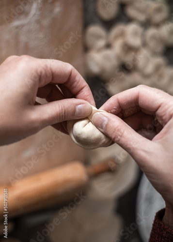 A woman in the kitchen sculpts dumplings from dough with meat filling. Cooking delicious homemade dumplings