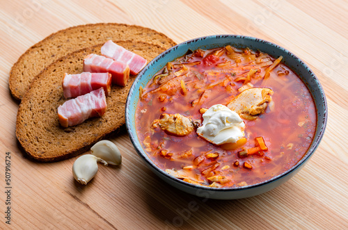 Ukrainian traditional cuisine. Red borscht with chicken and sour cream in a blue plate on a wooden background