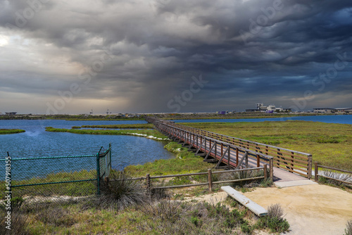 a long brown wooden bridge over a lush green marsh surrounded by vast blue ocean water with powerful clouds at sunset at Bolsa Chica Ecological Reserve in Huntington Beach California USA photo