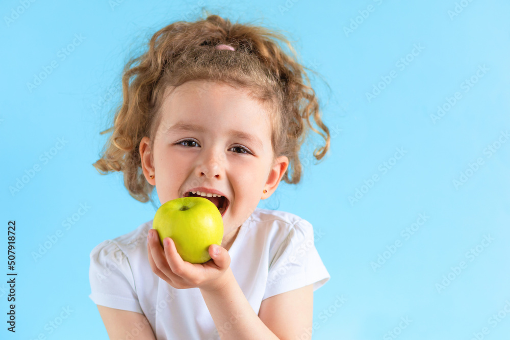 cute child smiling bites apple. nutrition for caries prevention. portrait of little girl with fruit on blue background. kid eating healthy food, snack. teeth, dental health, smile. children dentistry cute child smiling bites apple. nutrition for caries prevention. portrait of little girl with fruit on blue background. kid eating healthy food, snack. teeth, dental health, smile. children dentistry