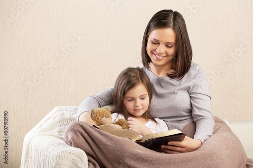 Happy mom and teen daughter smiling and reading interesting book while relaxing on weekend day at home