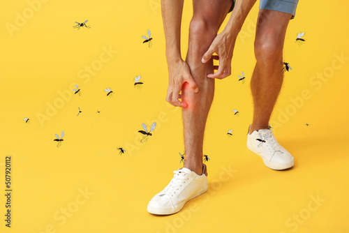 Young man scratching himself and many mosquitoes on yellow background