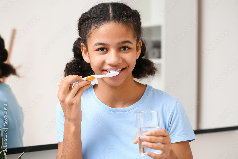 African-American teenage girl with glass of water brushing teeth in bathroom African-American teenage girl with glass of water brushing teeth in bathroom