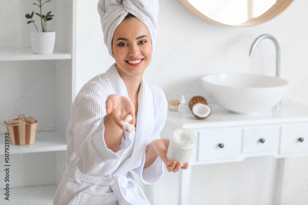 Young woman with jar of coconut oil in bathroom - obrazy, fototapety, plakaty 