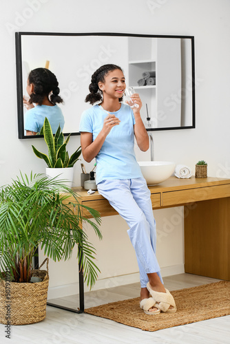 African-American teenage girl with toothbrush and glass of water in bathroom