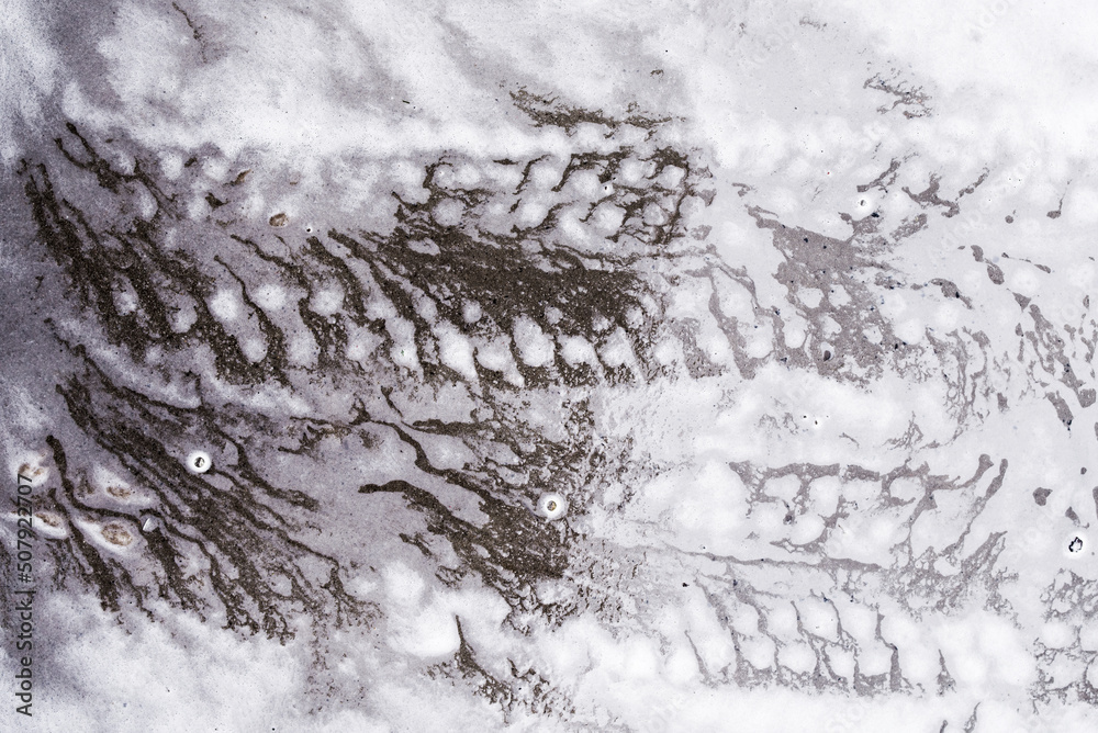 Car tire marks on wet pavement on soapy white foam from detergents at a car wash. Texture background.