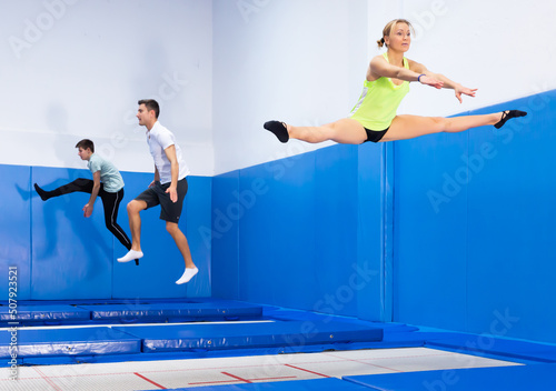 Female gymnast jumping on professional trampoline, practicing middle split in hop jump..