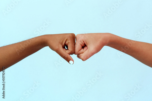 Black African American woman and white Caucasian woman punching on a blue background. Partnership and cooperation agreement, multiracial diversity and immigration concept. Stop racism.