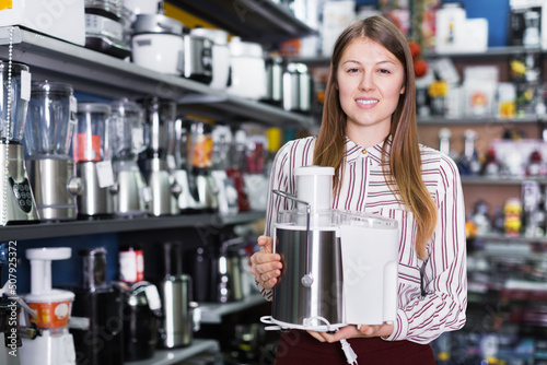 Positive salesgirl suggesting kitchen machine in store of a household appliances