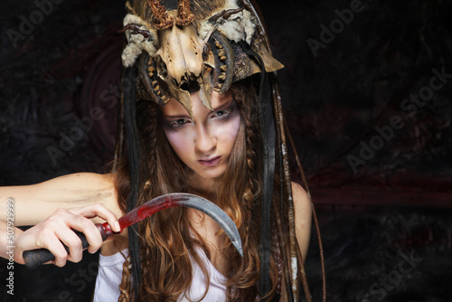 Young woman with aggressive make-up holding a sickle. Halloween.