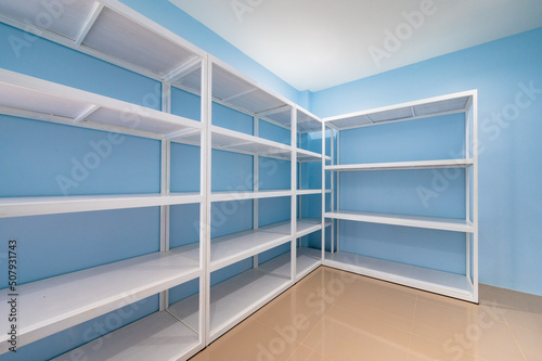 Empty white shelves in blue storage room © Kobchai M.